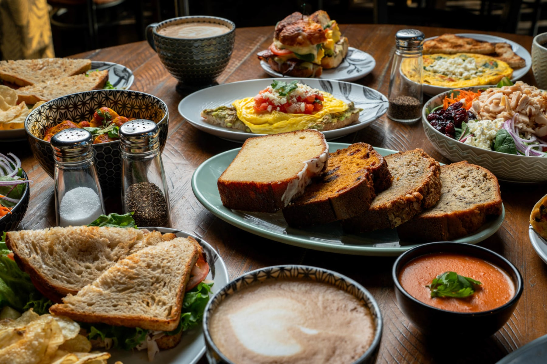 Food spread at Oasis Cafe with sandwiches, omelets, salad, tomato soup, and lattes