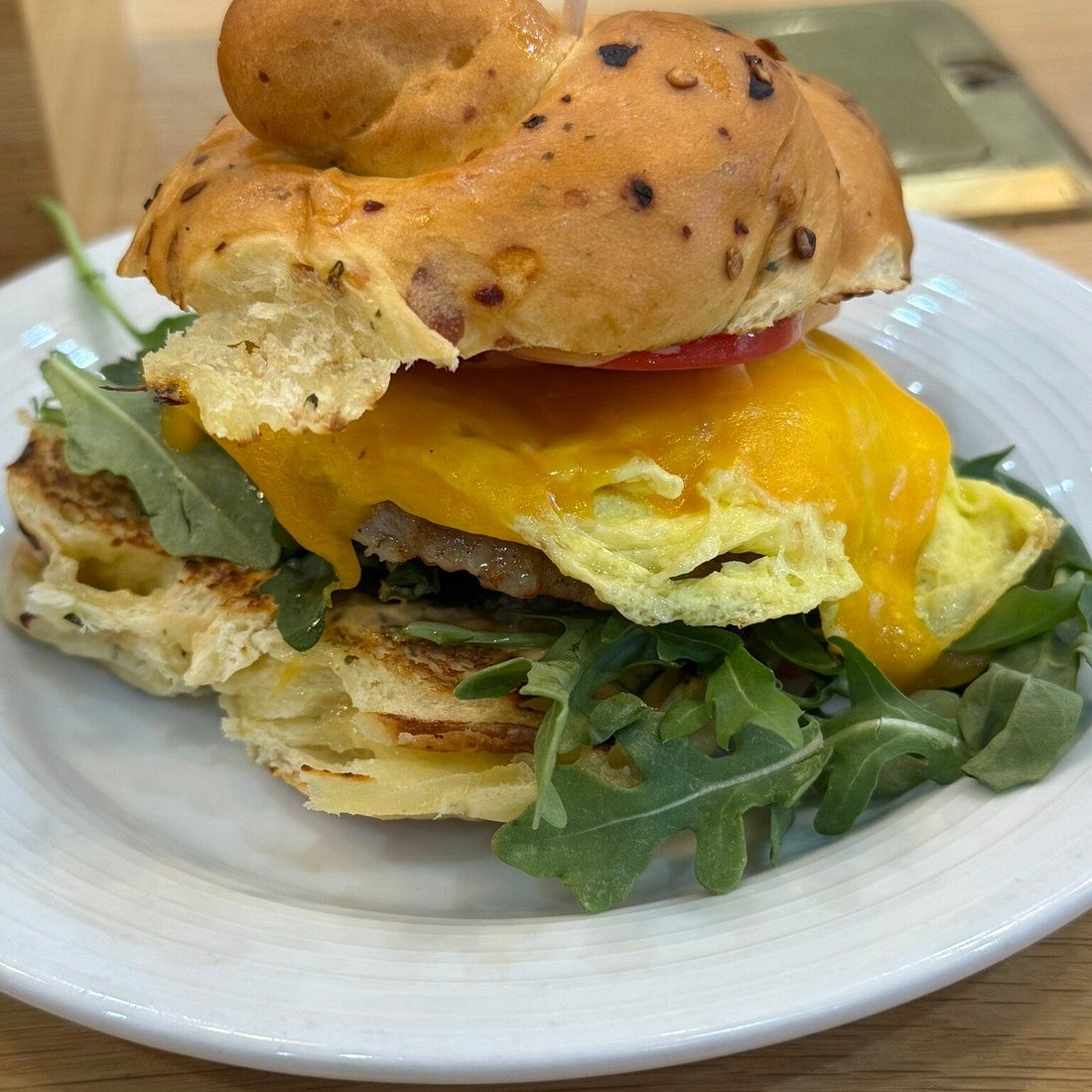 Hella Stella breakfast sandwich with melted cheddar, egg, sausage, tomato, and arugula on a Stella bun from Ancora in Madison