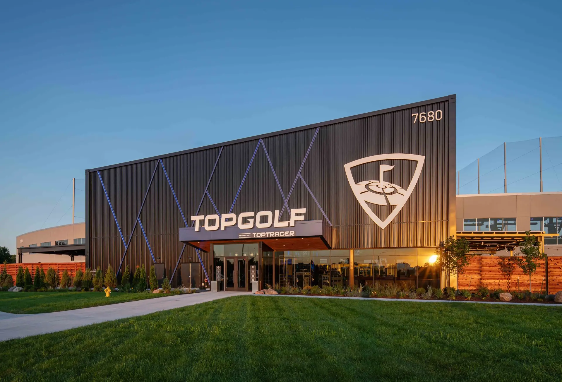 Multi-level Topgolf hitting bays at dusk overlooking lit target greens on the driving range