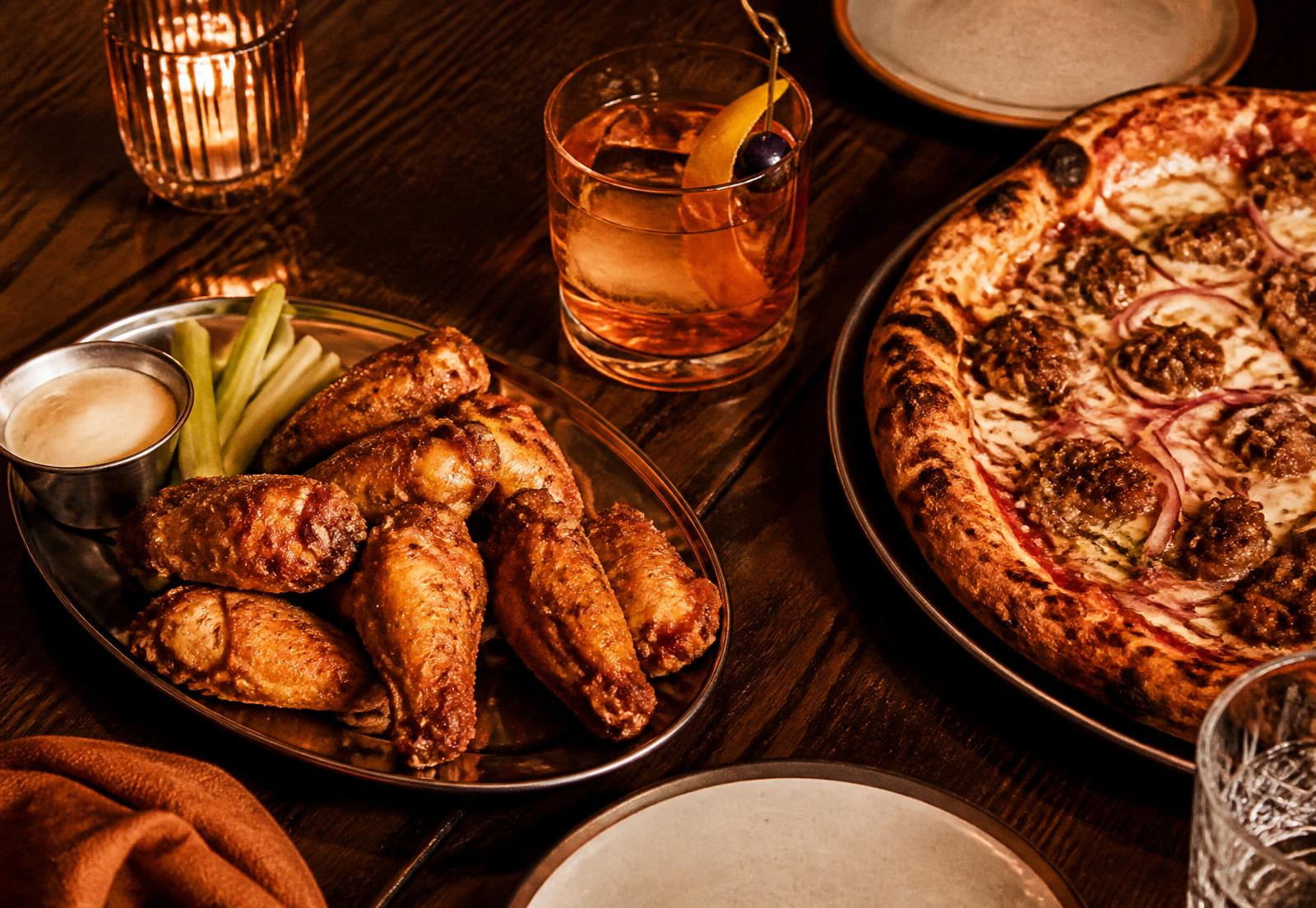 Wings, a brandy old fashioned and a pizza on a walnut supper club table